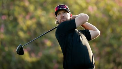 Golfer swings club in black shirt