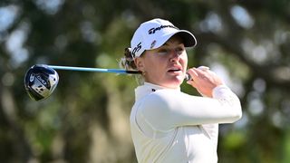 Woman swings golf club on course